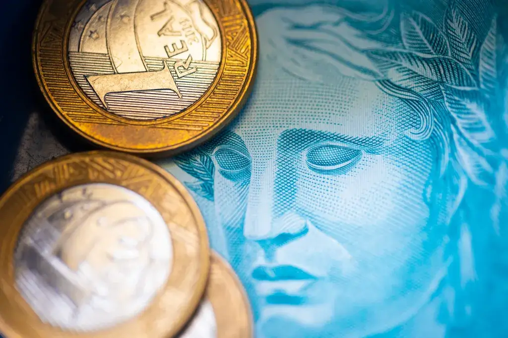 Moedas de real sobre cédula brasileira, simbolizando a moeda física em circulação.